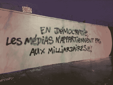 “Mur avec barbelés sur le dessus où il est écrit: «En démocratie,
les médias n'appartiennent pas aux
milliardaires»”